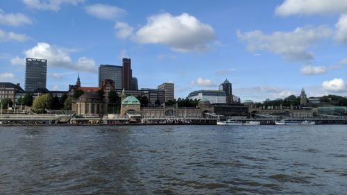 View of buildings by river against cloudy sky