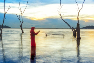 Rear view of woman standing by sea against sky during sunset