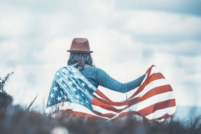 Rear view of woman sitting on flags against sky