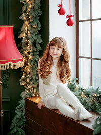 Happy young girl sitting by the window and christmas tree