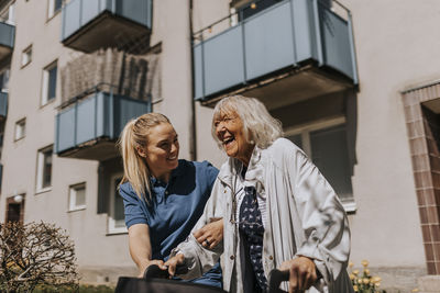 Smiling female caregiver helping happy senior woman walking outside building