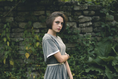 Young woman looking away while standing against wall