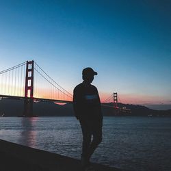 Silhouette man standing on bridge over river against sky