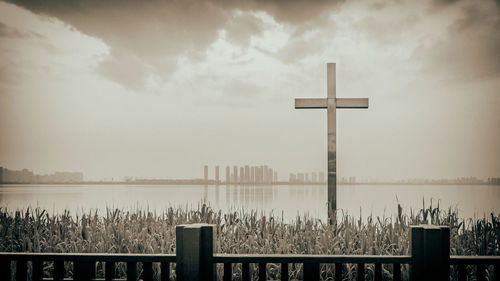 Cross on lake against sky