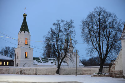 Bare trees in front of church against sky during winter