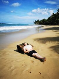 Man lying down on sand at beach against sky