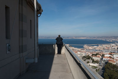 Man standing on retaining wall by sea against sky