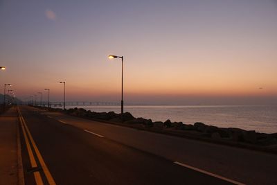 Road by sea against sky at sunset