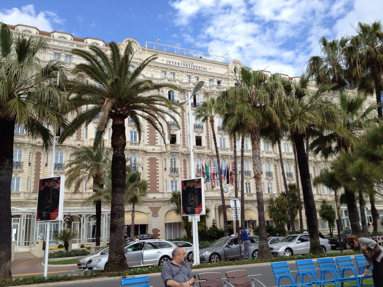 building exterior, architecture, built structure, tree, sky, car, transportation, mode of transport, palm tree, land vehicle, street, cloud - sky, incidental people, city, day, road, travel, outdoors, cloud, building