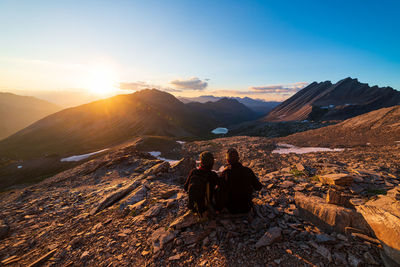 Rear view of woman sitting on mountain against sky