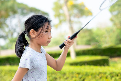 Girl holding badminton racket while standing by plants