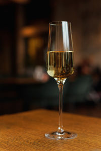 Glass of champagne standing on wooden table in soft focus on naturally blurred dark background