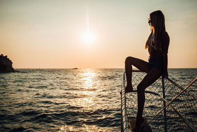 Woman in sea against sky during sunset