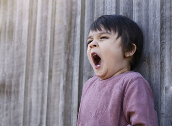Boy yawning while looking away against wall
