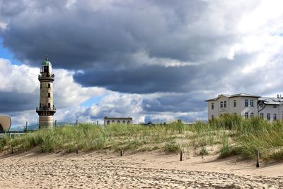 Lighthouse on beach against cloudy sky