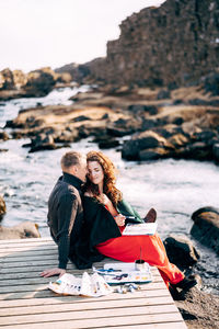 Full length of couple sitting on boardwalk by river