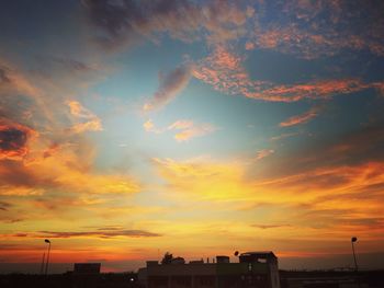 Silhouette city against dramatic sky during sunset