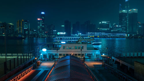 Illuminated modern buildings by river against sky in city at night