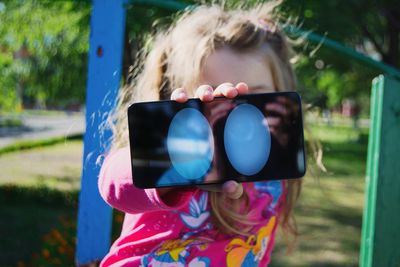 Close-up of girl showing blue ellipse shapes on mobile phone at park