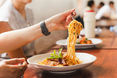 Woman eating spaghetti with friend in restaurant.