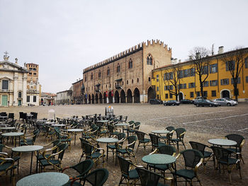 Chairs and tables in town by buildings in city against sky