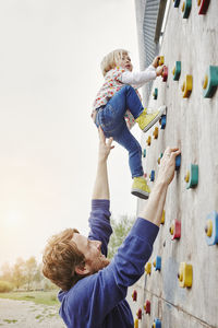 Girl climbing on a wall supported by father
