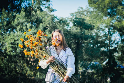 Young woman holding umbrella standing by flowering plants