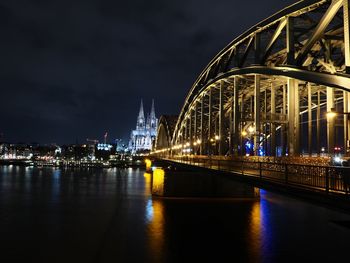 Illuminated bridge over river against buildings at night