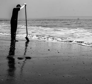 Boy holding shovel while standing at beach against sky