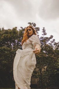 Young woman standing by tree against sky