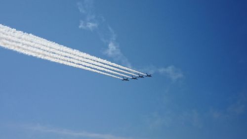 Low angle view of airplanes flying against blue sky