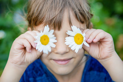 Close-up of boy covering eyes with flowers