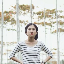 Thoughtful young woman standing against trees