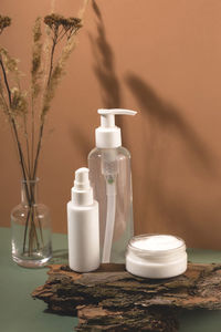 Close-up of cosmetics bottles on the table next to vase with dry flowers