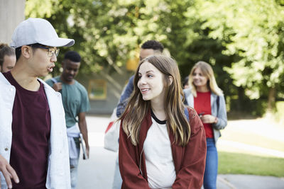 Smiling friends talking while walking at university campus on sunny day