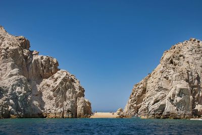 Rock formations by sea against clear blue sky