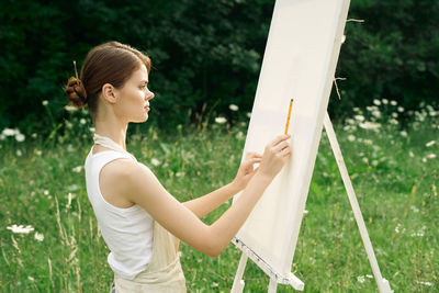 Side view of young woman holding sunglasses on field