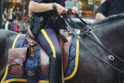 Midsection of police officer riding horse in city