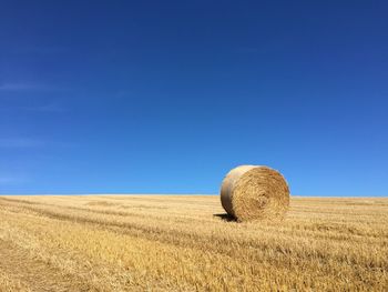 Hay bales on field against clear blue sky