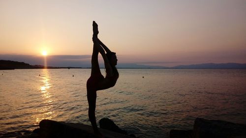 Silhouette woman exercising by sea during sunset