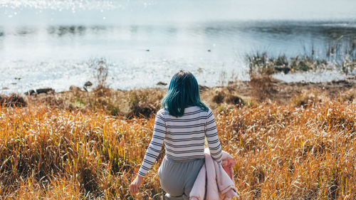 Rear view of woman walking on field against lake