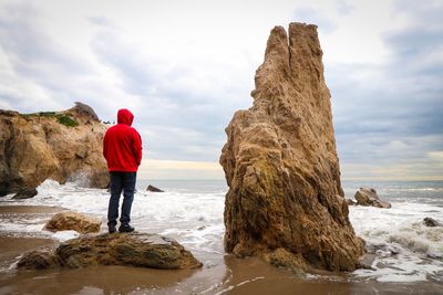 Rear view of man standing on rock at beach against sky