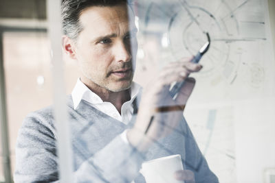 Portrait of architect checking construction plan on glass pane in office