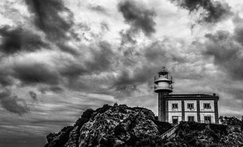 Low angle view of building on cliff against cloudy sky