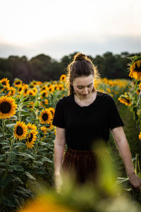 Portrait of young woman with sunflower on field against sky