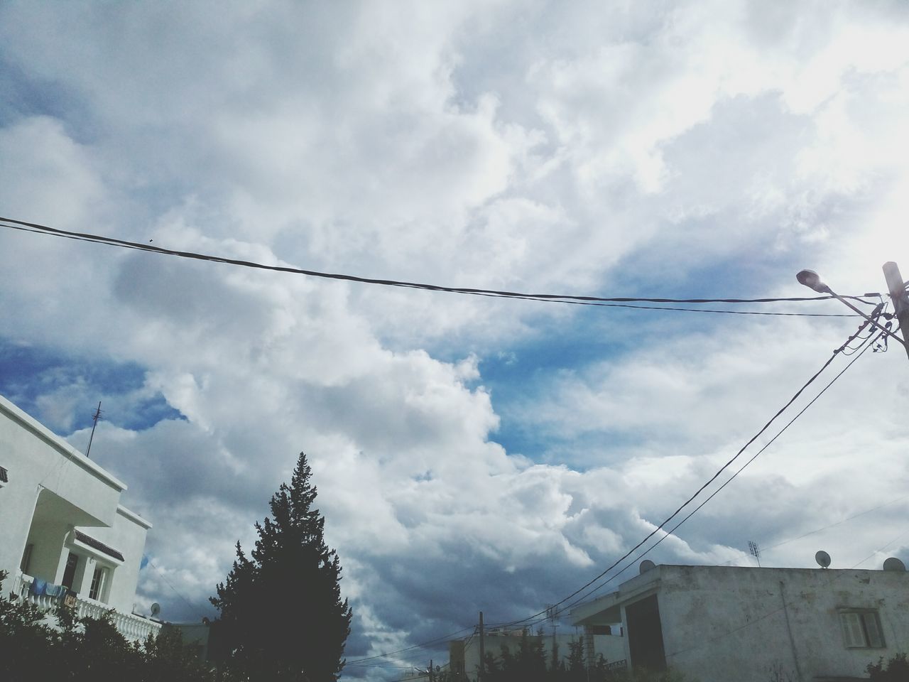 sky, low angle view, cloud - sky, architecture, built structure, building exterior, cloudy, power line, cable, connection, electricity pylon, cloud, power supply, electricity, weather, house, fuel and power generation, overcast, residential structure, day