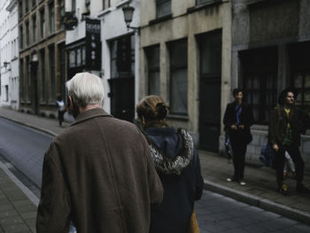 Rear view of people walking on sidewalk in city