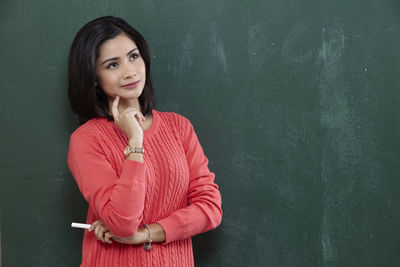 Thoughtful female teacher standing by blackboard