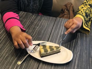 Cropped hands of girls having cake slice from plate on table