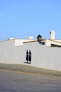 Rear view of woman walking by building against clear blue sky